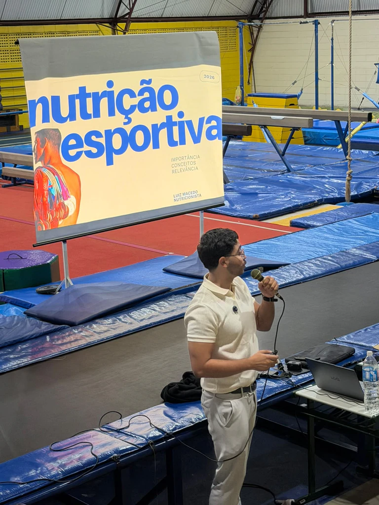 Luiz Macedo com microfone diante do slide “nutrição esportiva: importância, conceitos, relevância”, em um ginásio
